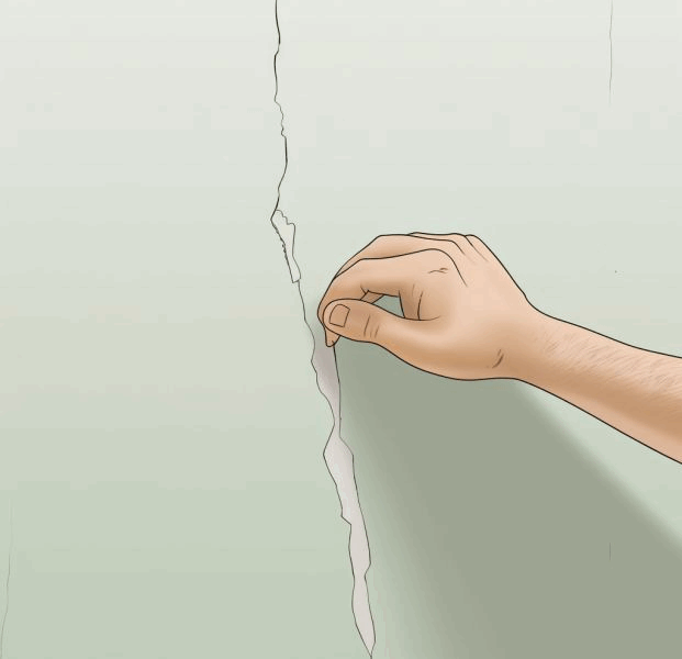 Hand peeling cracked drywall plaster from damaged interior wall
