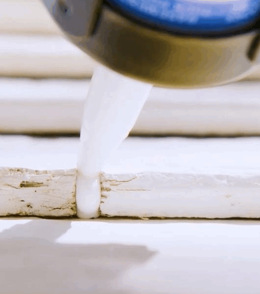 Applying white caulk to seal cracked window frame gap