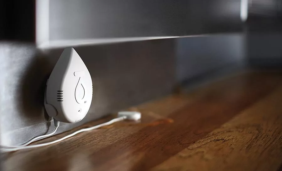 Smart water leak detector plugged near baseboard on floor